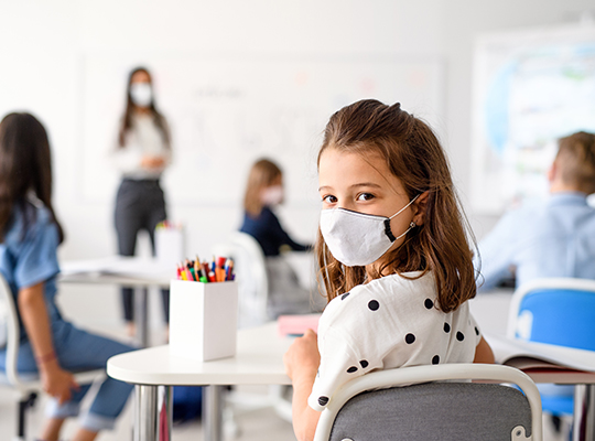 teacher instructs students in classroom wearing masks