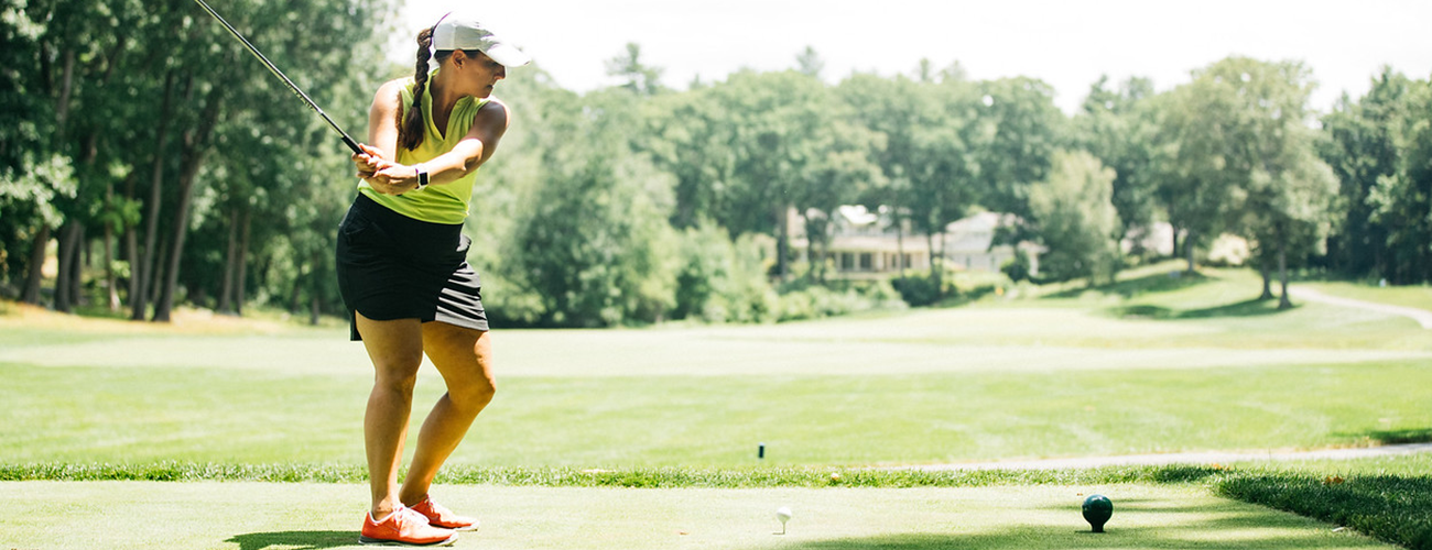 woman swinging golf club on grass