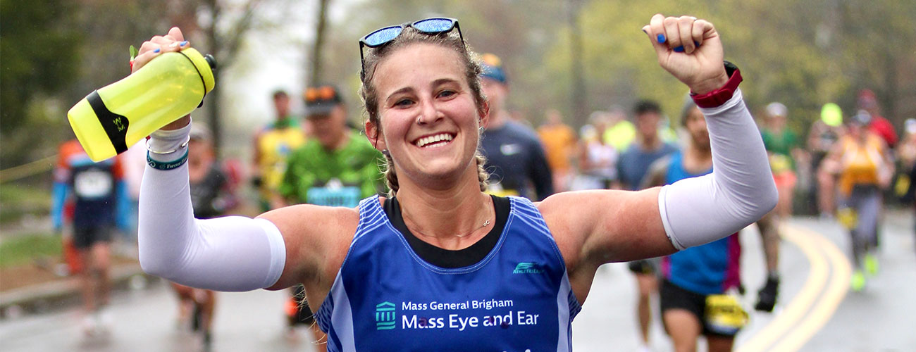 team eye and ear marathon female runner smiling with her hands in the air